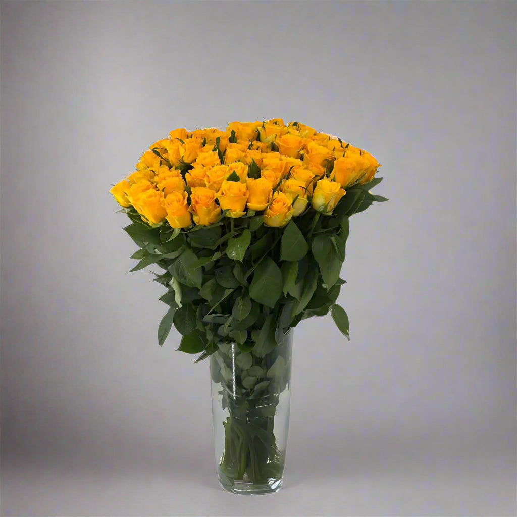 Bouquet of yellow roses in a clear vase on a gray background