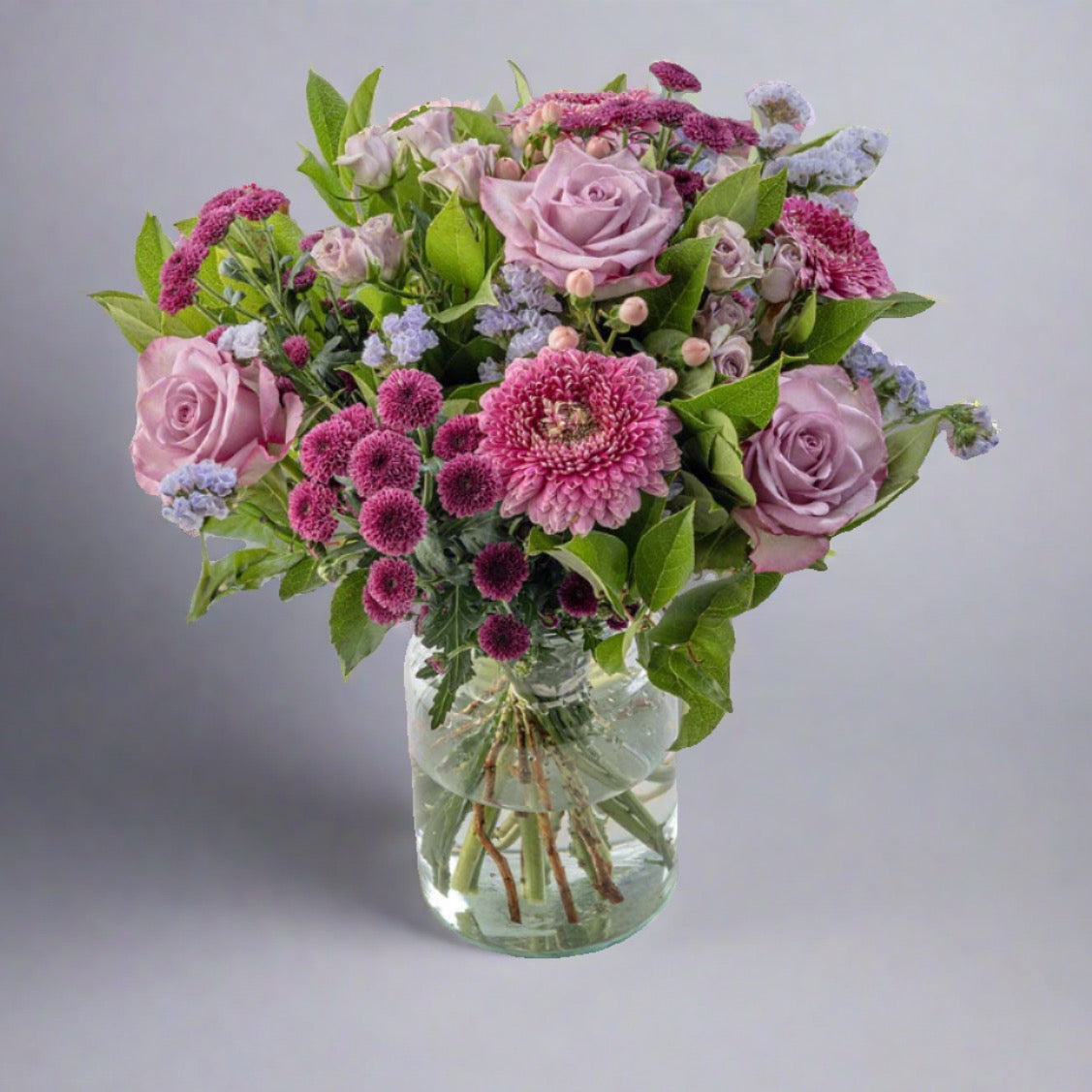A floral bouquet containing roses, germini, button mums, spray roses, hypericum, and statice arranged in a clear vase.