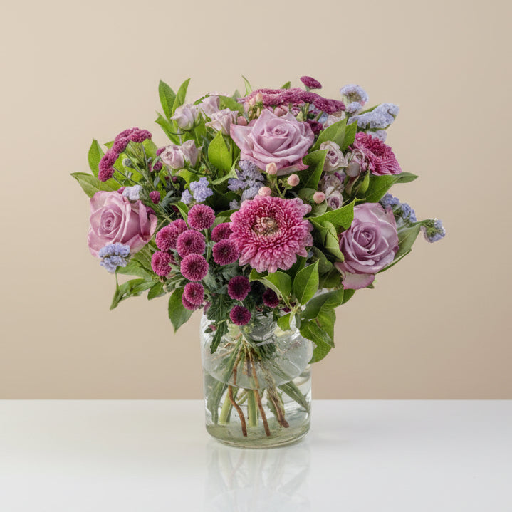 A floral bouquet containing roses, germini, button mums, spray roses, hypericum, and statice arranged in a clear vase.