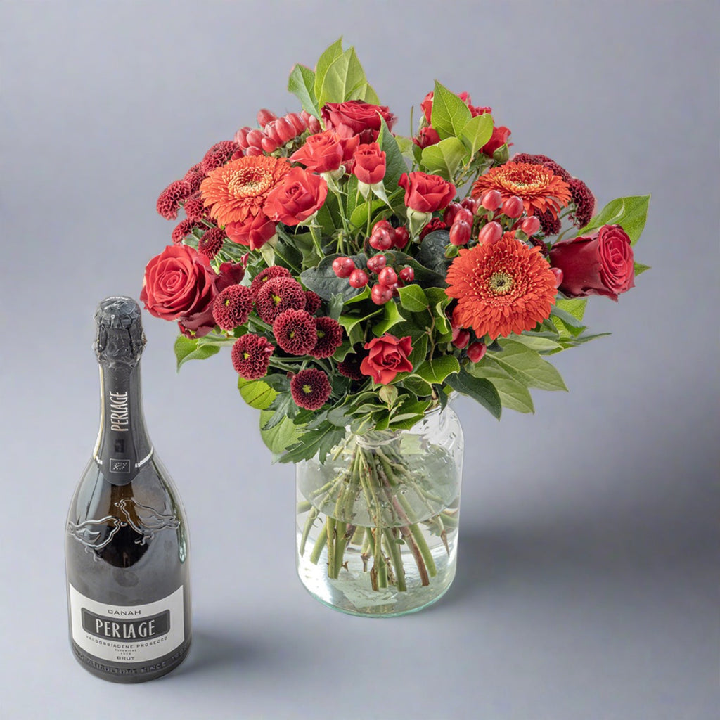 Red flower bouquet in a glass vase with bottle of organic periage prosecco