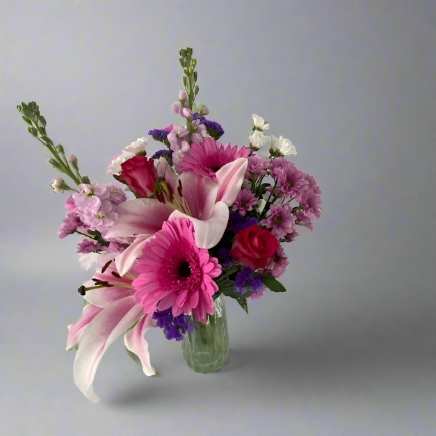 A vibrant bouquet of flowers including roses, lilies, and Gerbera daisies in a clear vase, arranged to create a visually pleasing floral display.