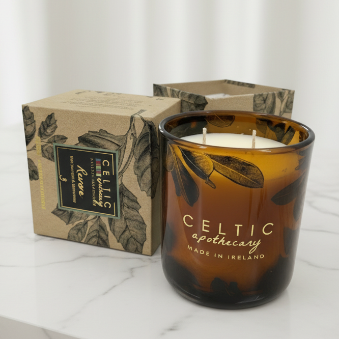 Candle with 'Celtic Apothecary' branding next to its packaging on a marble surface.