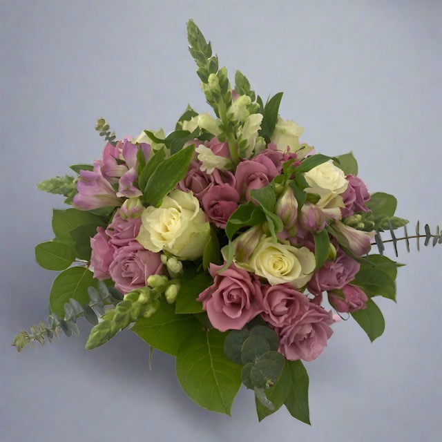 A floral table topper arrangement featuring a mix of purple, pink, and white flowers with green foliage.