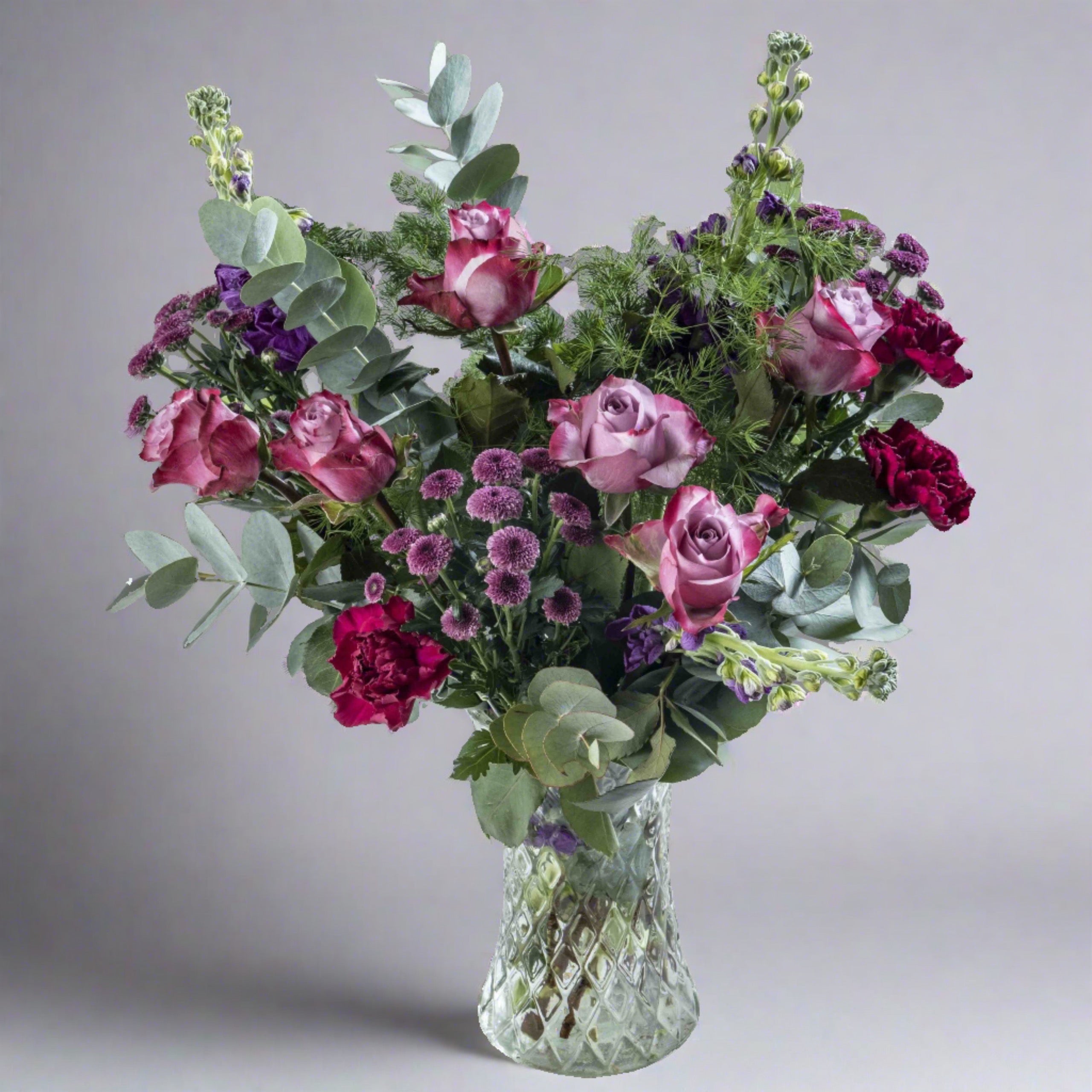 A vibrant flower bouquet featuring a variety of flowers including roses and other greenery, arranged in a clear vase.