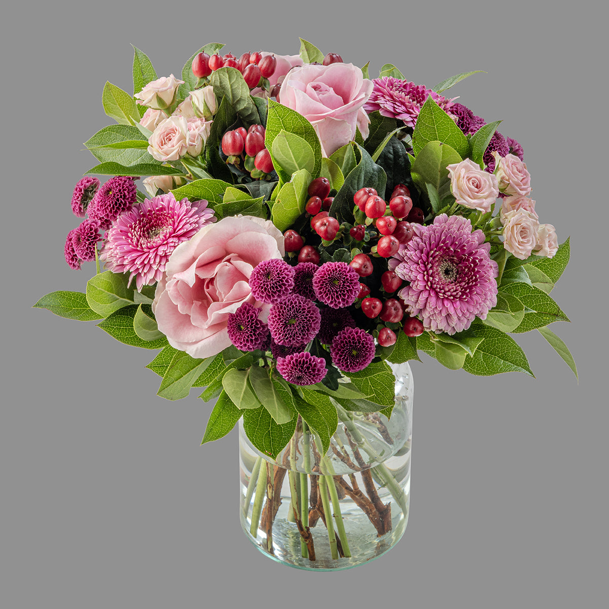 A bouquet of flowers featuring pink roses, purple gerberas, and red Hypericum berries, arranged in a clear glass vase.