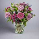 A floral bouquet containing roses, germini, button mums, spray roses, hypericum, and statice arranged in a clear vase.