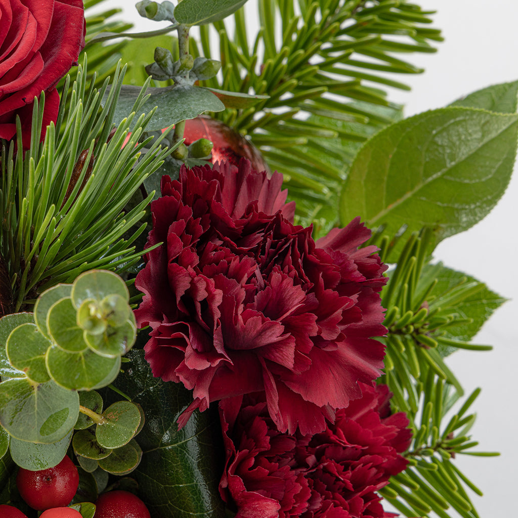Close up view of red rose and green florals from Christmas reds tabletop bouquet