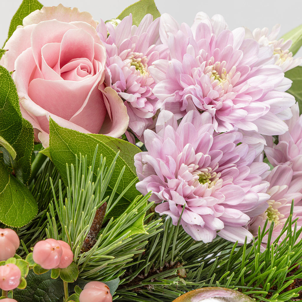 Close up view of a pink rose and other floral elements from the Christmas pink roses bouquet in a glass vase