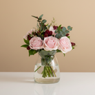 Bouquet of pink roses and greenery in a clear vase on a white background