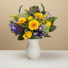 Bouquet of yellow and purple flowers in a white vase on a beige background