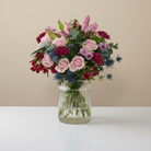 Bouquet of flowers in a clear vase on a white surface with a beige background