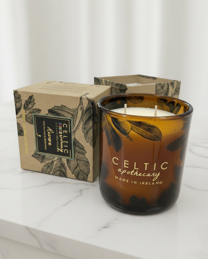 Candle with 'Celtic Apothecary' branding next to its packaging on a marble surface.