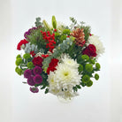 Colorful Christmas bouquet of flowers including red roses, greenery, and white flowers on a light gray background