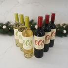 Bottles of eco wine with green and red labels on a white surface with Christmas decorations.