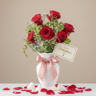 Bouquet of red roses in a white vase with a pink ribbon, accompanied by a 'Happy Valentine's Day' card on a beige background.