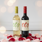Two wine bottles labeled 'eco' on a surface with rose petals and blurred lights in the background